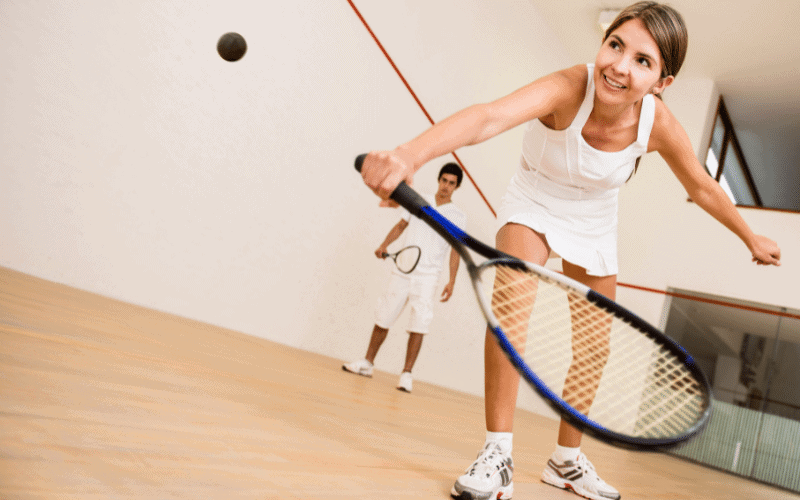 A group of young squash players are practicing and receiving training in a well-lit indoor court, with coaches instructing and guiding them