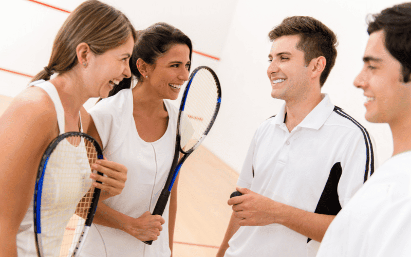 A group of squash players gather around a rule board, discussing and pointing at the regulations. Additional resources are stacked nearby, and a sense of community and learning is palpable in the air