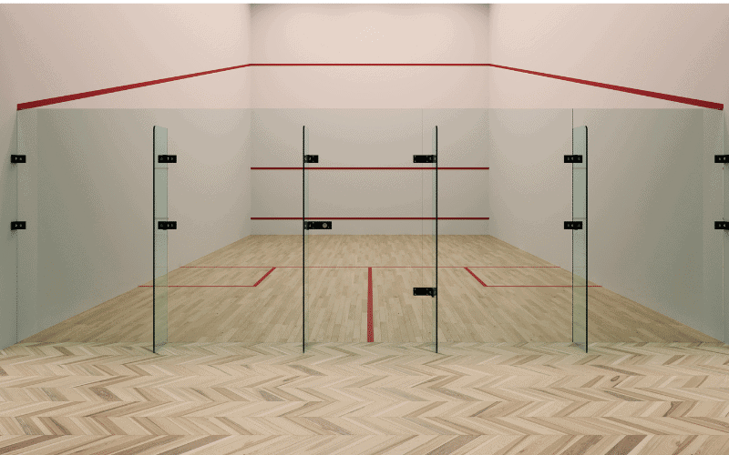 A squash court with regulation markings and equipment, including a racquet, ball, and protective eyewear